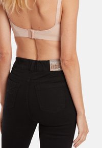 Soutien-gorge rose clair avec des bretelles ajustables et une fermeture à crochets, associé à un jean noir taille haute avec une étiquette texturée et des poches arrière.