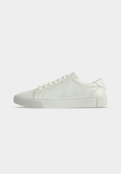 Λευκό δερμάτινο sneaker χαμηλού τύπου με λευκά κορδόνια και υφή στη λαστιχένια σόλα, εμφανιζόμενο από το πλάι σε απλό φόντο.