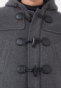 Manteau duffle en mélange de laine grise avec une fermeture à brandebourg, de grandes poches avant et une capuche. Tissu texturé avec une finition lisse.
