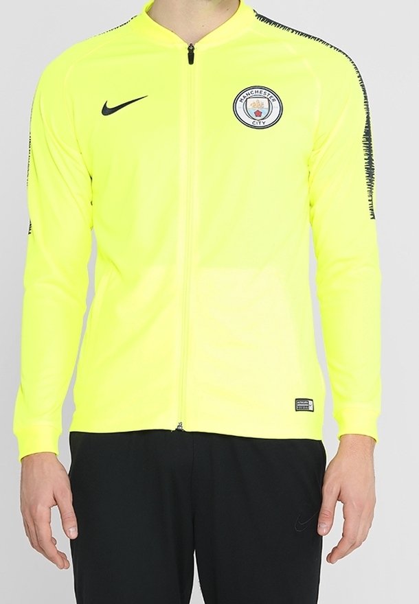 Yellow zip-up jacket with long sleeves and black accents. Features Manchester City logo on chest and a slim, athletic fit.