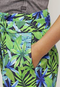 Tropiska mönsterbyxor i livfulla gröna och blå nyanser med en mörk bakgrund. Har en bred midjeband och sidofickor.