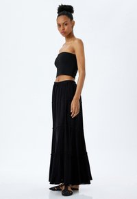 Top de tubo negro con textura acanalada acompañado de una larga y fluida falda maxi negra de volantes. La falda presenta un diseño fruncido y una cintura con cordón.