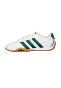 Zapatilla deportiva blanca con franjas verdes, con parte superior de cuero texturizado, suela exterior de goma de color marrón claro y cuello acolchado para mayor comodidad.
