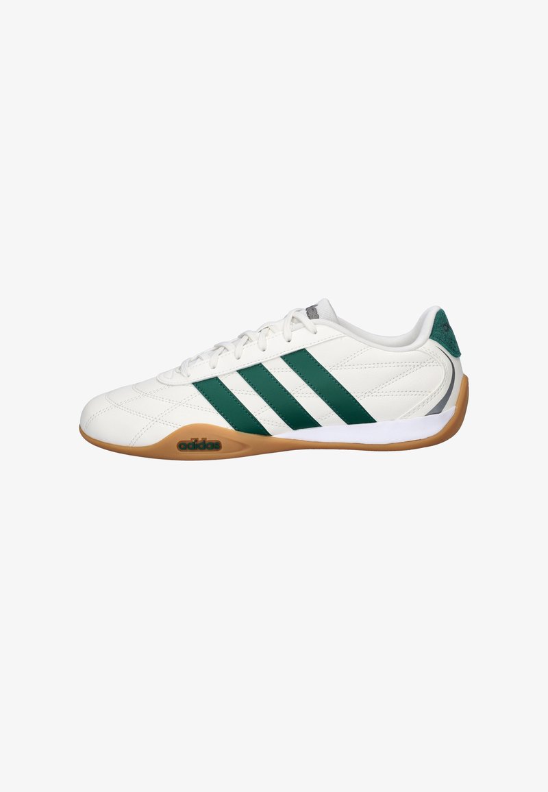 Zapatilla deportiva blanca con franjas verdes, con parte superior de cuero texturizado, suela exterior de goma de color marrón claro y cuello acolchado para mayor comodidad.