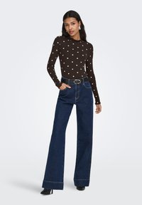 Brun ribstrikket langærmet top med hvide prikker, kombineret med vidde-blå denim jeans. Sort bælte og sorte sko med hæl fuldender outfittet.