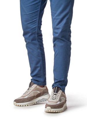 Herrensneaker aus beigem und braunem Wildleder mit strukturiertem Mesh-Obermaterial, dicker weißer Sohle und schwarzen Schnürsenkeln, kombiniert mit blauen Slim-Fit-Hosen.