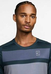 Camisa atlética de manga corta para hombre en color teal con rayas horizontales en gris oscuro y gris claro. Textura suave, escote redondo y detalle del logo.