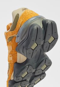 Orange textile and mesh sneaker with a thick black rubber sole and translucent accents, featuring a textured upper and prominent branding.