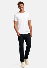 Weißes Baumwoll-T-Shirt mit rundem Halsausschnitt, kombiniert mit schwarzen Hosen und beigen Sneakers, mit einem lockeren Schnitt und minimalistischen Design.