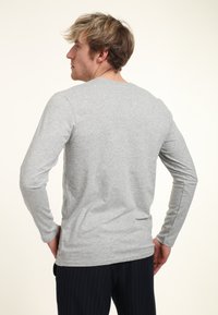 Dlouhý rukáv šedého trička vyrobeného z jemné bavlny, s kulatým výstřihem, rovný střih a jemnými bočními rozparky pro snadný pohyb.