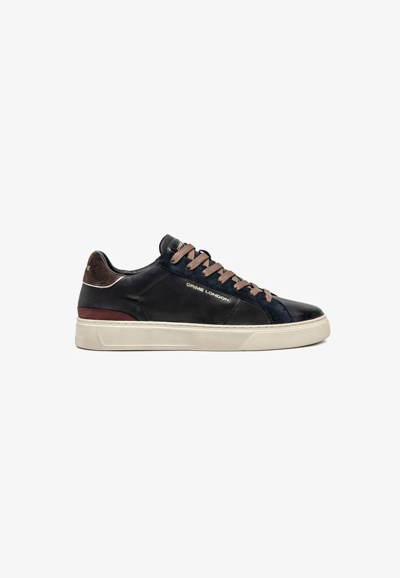 Sneaker nera a bassa cima con lacci marroni, linguetta in suede sul tallone, suola bianca e logo "Crime London" sulla parte laterale.