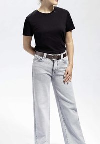 T-shirt en coton noir associé à un jean en denim à jambes larges gris clair. Une ceinture tissée marron ajoute une touche de détail. Design simple avec une coupe classique.