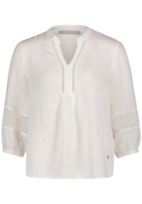 Camicia bianca con scollatura a V, caratterizzata da inserti in pizzo decorativo sulle maniche e una vestibilità ampia. Il tessuto ha una consistenza liscia e leggera.