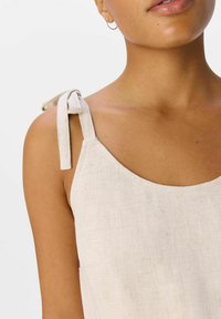 Débardeur en lin beige clair avec des bretelles réglables à nouer, présentant un col simple et un tissu texturé.