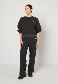 Black pullover sweatshirt with textured fabric and ribbed hem, paired with matching black sweatpants featuring a side logo detail.