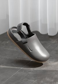 Sive slip-on cipela s glatkim, mat završetkom, koja ima stražnji remen i teksturiranu đon. Gumeni materijal s minimalnim dizajnom.