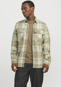 Geruite blouse met lange mouwen in lichtbruine en groene tinten, met twee borstzakken en een knoopsluiting aan de voorkant. Gepaard met een bruine T-shirt.