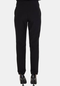 Pantaloni neri a sigaretta con vita elastica, realizzati in tessuto liscio, con vestibilità slim fino alla caviglia, indossati con scarpe con tacco alto.