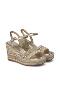Sandales compensées avec des brides dorées métalliques, texture tressée et une plateforme texturée. La fermeture à boucle et les semelles rembourrées améliorent le confort.