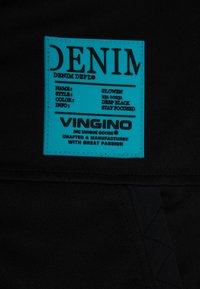 Etiqueta de denim azul brillante sobre tela negra con detalles del estilo St. Owen, color Negro Profundo y marca Vingino.
