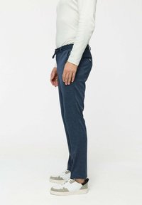 Navy blue pants with a slim fit, elastic waistband, and side pockets. Paired with white sneakers featuring grey accents.
