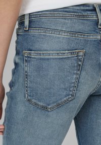 Lichtblauwe denimjeans met een klassiek vijfzakkenontwerp, zichtbare stiksels en een taps toelopende pasvorm. De stof heeft een gladde textuur.
