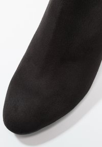 Bottine à talon en daim noir avec un bout pointu. Texture lisse et design élégant, avec un éclat subtil et une construction sans couture.