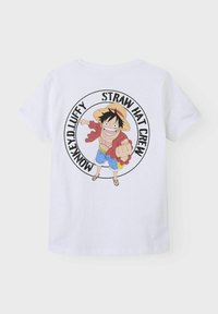 T-shirt en coton blanc avec un graphique circulaire noir. Le design présente un personnage de dessin animé portant un chapeau de paille, une veste rouge et un short bleu.