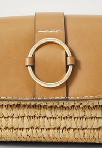 Tan leather handbag with a circular gold-tone hardware accent. Textured woven straw base, finished with white stitching.