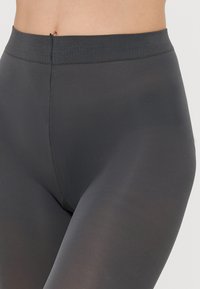 Grå leggings med høj talje lavet af strækbart stof med en glat tekstur og en bred elastisk talje. Har en tætsiddende silhuet.
