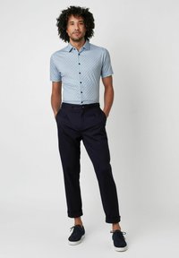 Hellblaues Kurzarmhemd mit geometrischem Muster, kombiniert mit dunkelblauen Hosen und dunkelblauen Sneakern, mit einer Knopfleiste.