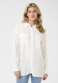 Camicia bianca con bottoni, due tasche sul petto, maniche lunghe e orlo arrotondato, realizzata in un tessuto leggero. Texture liscia, vestibilità casual.