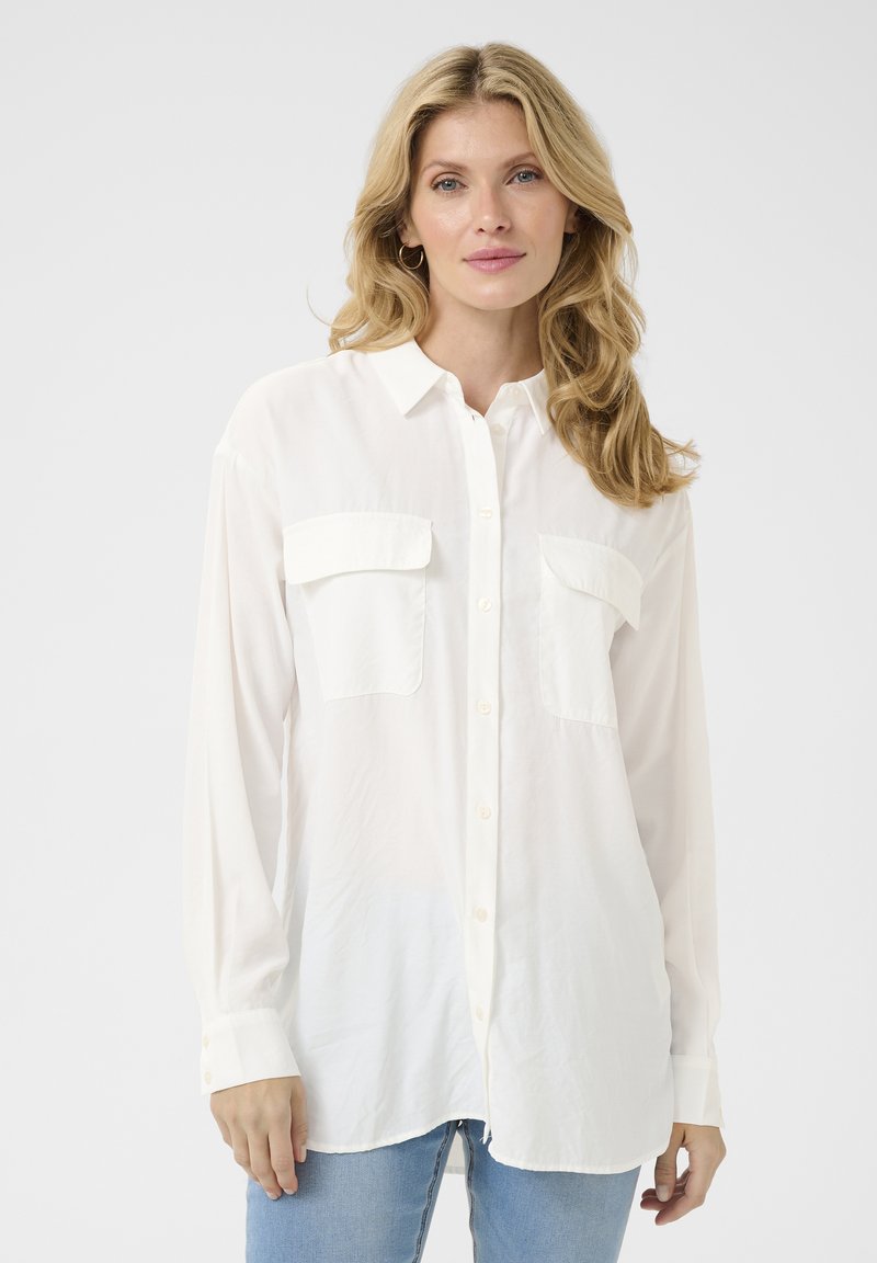 Camicia bianca con bottoni, due tasche sul petto, maniche lunghe e orlo arrotondato, realizzata in un tessuto leggero. Texture liscia, vestibilità casual.