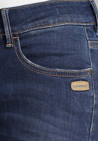 Vaqueros de mezclilla azul oscuro con un corte de media altura, costuras en contraste, un bolsillo delantero y una etiqueta de cuero con la marca en la cintura.