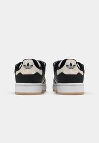 Black and beige suede sneakers with three black stripes, white rubber sole, and blue accents at the collar, featuring a logo on the heel.