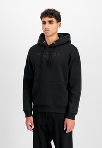 Sudadera negra hecha de una mezcla de algodón, con capucha ajustable, bolsillo canguro frontal y un sutil estampado de logo en el pecho. Textura suave.