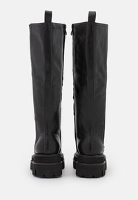 Botas de cuero negro hasta la rodilla con textura suave, cremallera lateral y suelas de goma gruesas. Acentos reforzados en el tacón y en el tubo.
