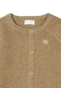 Beige stickad cardigan med rund halsringning, tre knappar och en liten broderad logotyp på vänster bröst. Slät textur genom hela plagget.