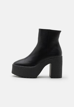 Botte de cheville en cuir noir avec un talon plateforme texturé épais et un bout rond sur fond blanc uni.