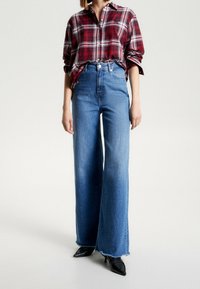 Rudternet skjorte i rød og hvid, båret over høj taljede, vidde ben blå denimjeans med frynsede kanter; kombineret med sorte spidse hæle.