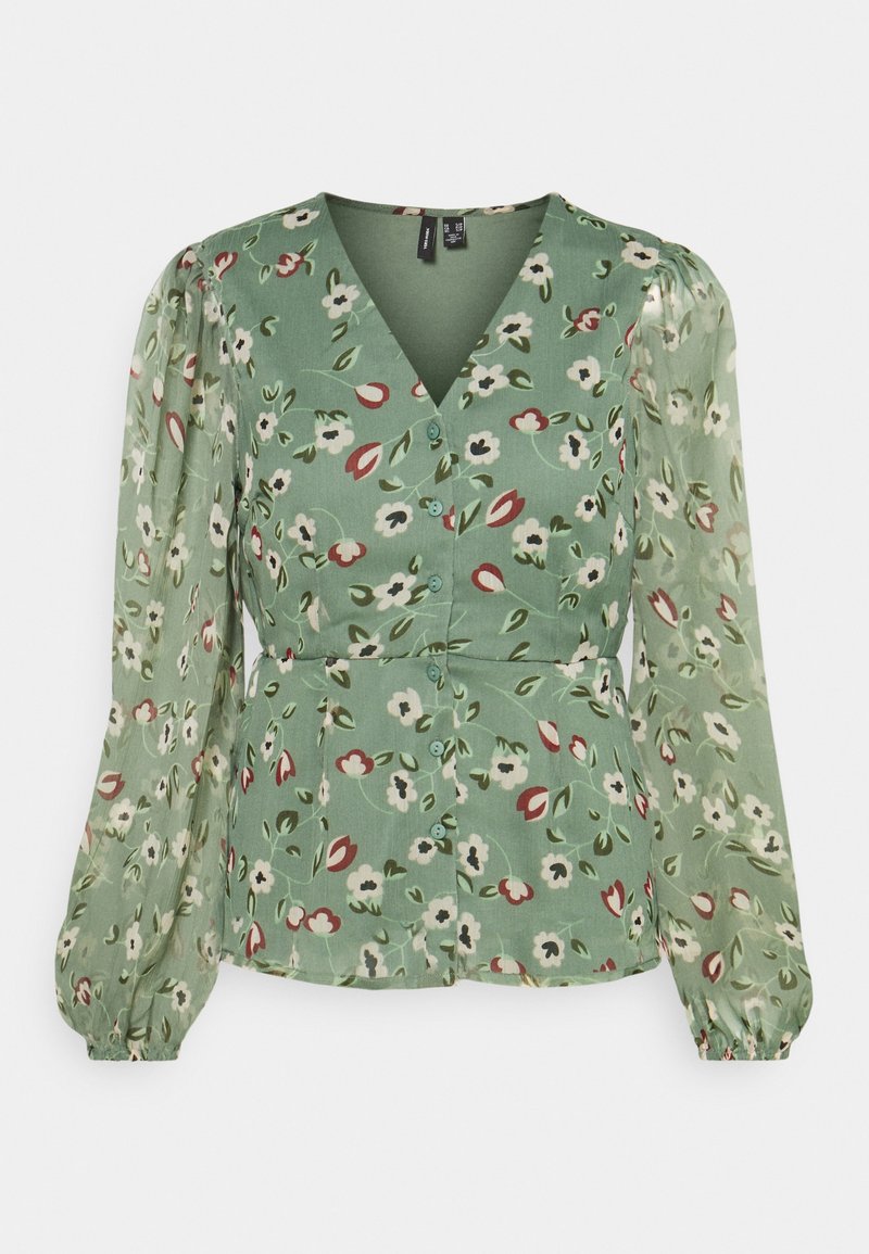 Blouse verte à fleurs avec col en V, manches longues transparentes bouffantes, boutons à l'avant et taille cintrée.