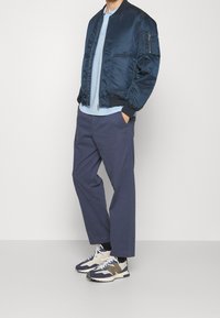 Marinblå satin bomberjacka, ljusblå polo t-shirt, marinblå byxor och flerfärgade sneakers. Jackan har dragkedja och sidofickor.