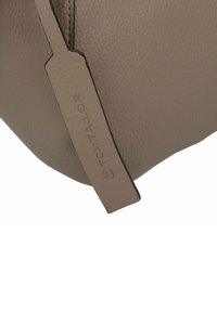 Bolso de imitación de cuero beige que presenta una superficie texturizada, forma redondeada y un etiquetado de logo destacado.