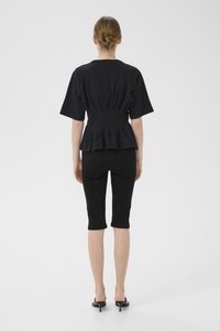 Svart kortermet topp med plisserte detaljer bak, kombinert med svarte knelengde leggings. Modellen går med svarte hælsandaler. Enkelt design, tettsittende stil.