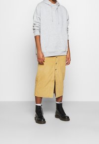 Ljust grå hoodie med en kenguruficka, kombinerad med en gul manchester midi-kjol med framknappar och en hög slits, bärs med svarta stövlar.