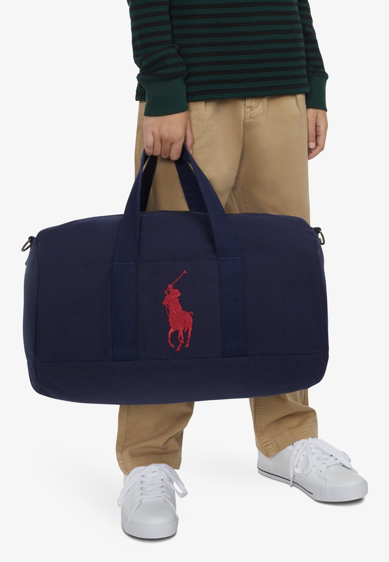 Bolsa de lona azul marino con logo bordado rojo, doble asa para llevar, diseño espacioso y cierre con cremallera para almacenamiento seguro.
