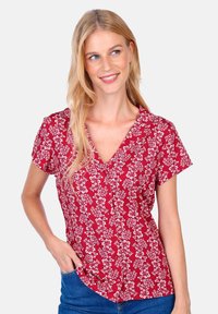 Red floral blouse with short sleeves, v-neckline, and button detail. Features a small white flower pattern throughout on a textured fabric.