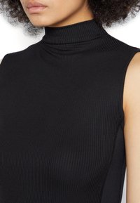 Top senza maniche nero a coste con colletto alto. Presenta un tessuto testurizzato e lati senza cuciture per un look aderente. Nessun ulteriore abbellimento.