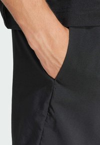 Black shorts with a side pocket; smooth texture, lightweight material, featuring a clean seam detail along the edge.