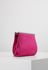 Fuchsiová semišová kabelka do ruky se stříbrným rámečkem a řetízkovým popruhem, má zaoblený tvar a hladkou texturu.